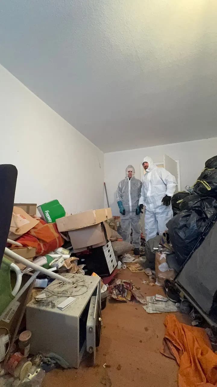 Mitarbeiter im Schutzanzug beim Räumen eines vollgestellten Zimmers