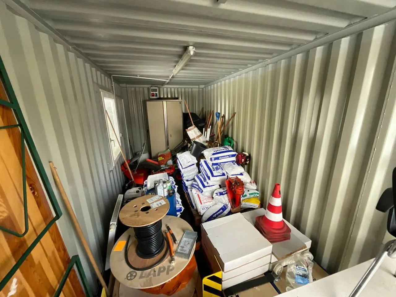 Container mit gestapelten Kartons, Kabeltrommeln und Material